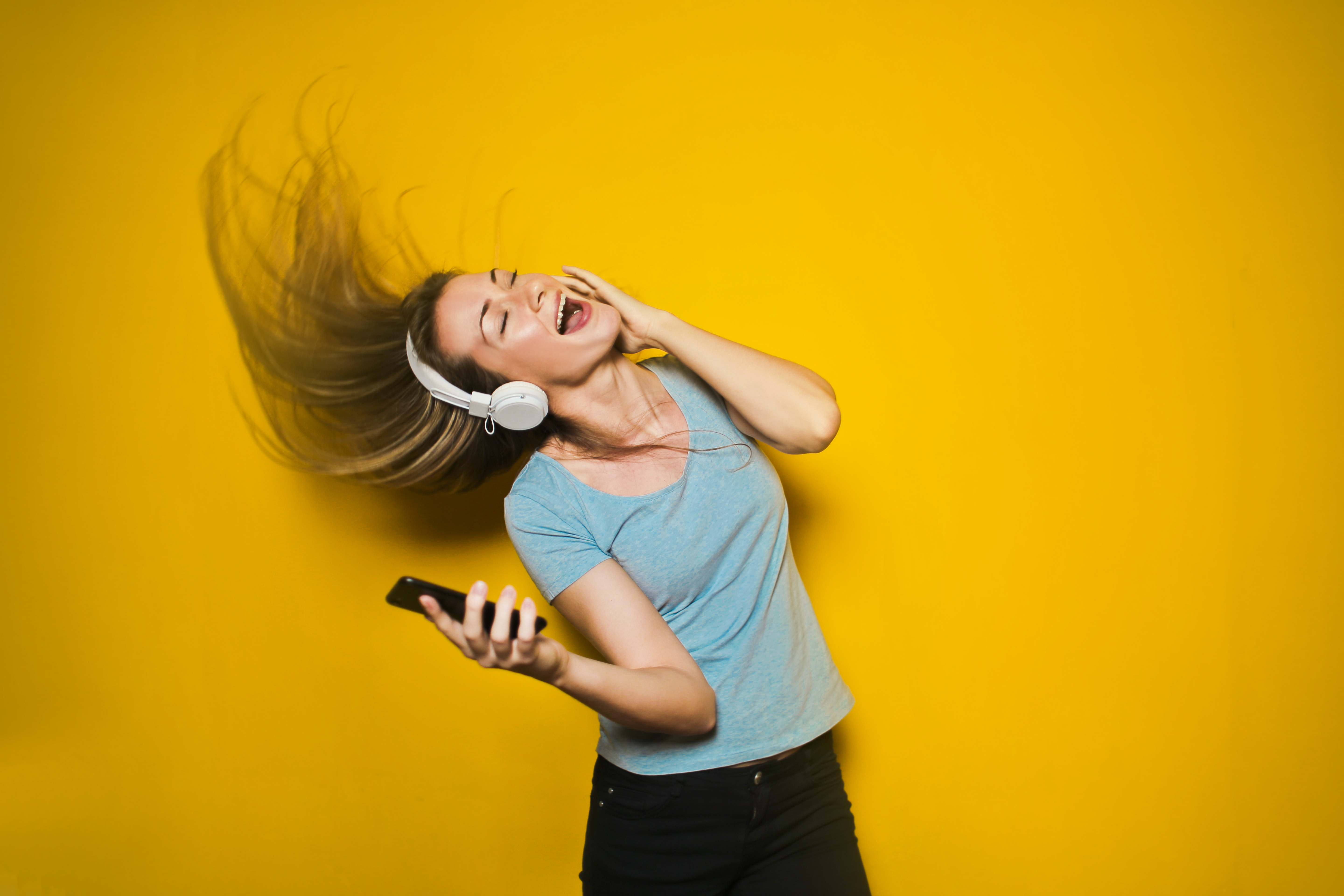 extrovert employees - girl dancing with earphones in with a yellow background